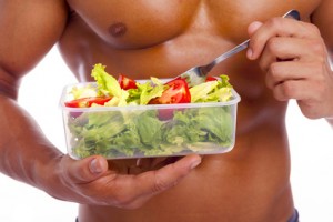 Close-up of a muscular man holding a bowl of fresh salad on a wh